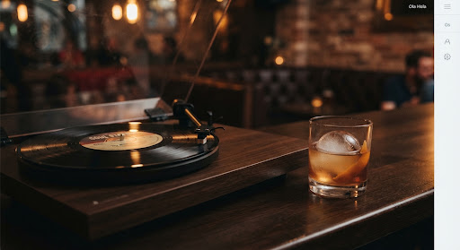 Close up photograph of a vintage vinyl turntable rotating a soul record beside a cocktail with a large hand-carved ice sphere in the low-lit, moody lounge of Ola Hola in Canterbury.